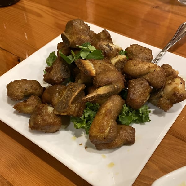 A plate of golden-brown fried pork ribs with fresh cilantro and lettuce on a wooden table.