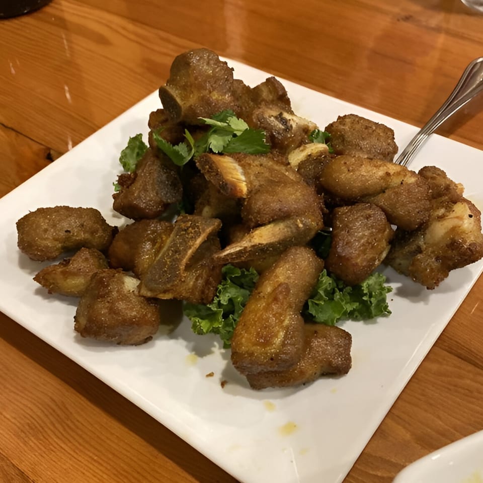 A plate of golden-brown fried pork ribs with fresh cilantro and lettuce on a wooden table.