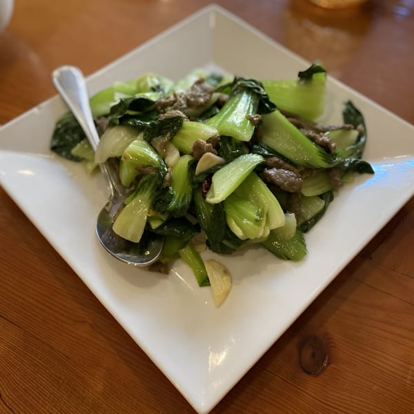 A white square plate filled with stir-fried bok choy and beef, served with a spoon.