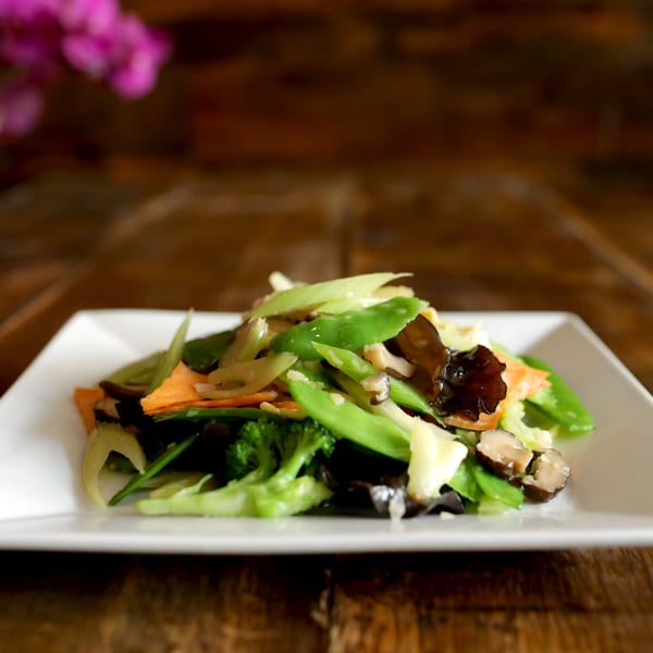 A vibrant stir-fry of mixed vegetables, including broccoli, carrots, and snow peas, on a white plate.