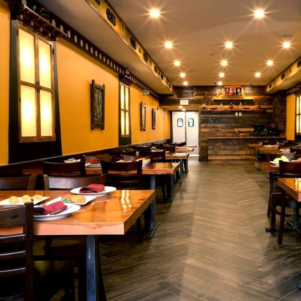 Warmly lit Tibetan restaurant interior with yellow walls, wooden tables, and decorative accents.