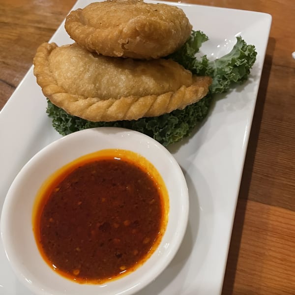 Two golden-fried Tibetan momos, one stacked on top of the other, with a side of chili sauce.