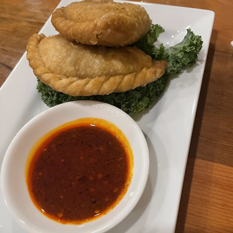 Two golden-fried Tibetan momos, one stacked on top of the other, with a side of chili sauce.