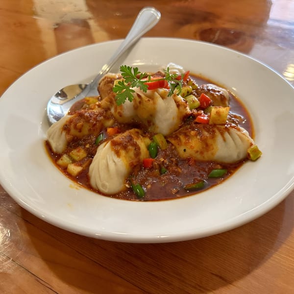 Tibetan momos in a rich, spicy sauce with diced vegetables and cilantro on a white plate.
