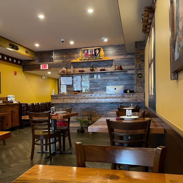 Interior of White Yak restaurant with wooden tables and chairs, yellow walls, and a rustic wooden counter.